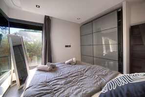 Ein modernes Schlafzimmer mit einem großen Bett, einem Spiegel und Blick auf Grünflächen.