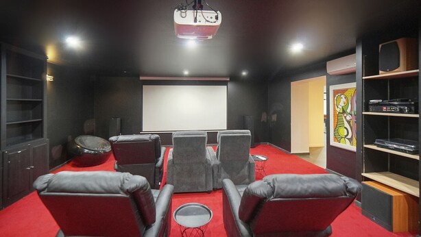 A home theater room with a red carpet, black and gray chairs, a large screen, and a projector. - Exceptional 9-Bedroom Villa in Mougins (Mougins)