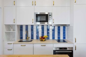 Eine moderne Küche mit weißen Schränken, einer Edelstahl-Mikrowelle, einem Waschbecken mit Goldarmatur und einem Bosch-Backofen.