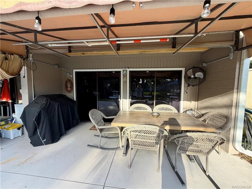 An outdoor patio with a table and chairs, a covered area with a fan, and a sliding glass door leading to the interior.