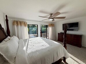 Ein Schlafzimmer mit Himmelbett, Deckenventilator, einem an der Wand befestigten Fernseher und Blick ins Freie durch eine Schiebetür.