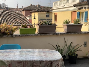Eine Terrasse mit Tisch und Stühlen, Blumentöpfen und einem Gebäude mit Ziegeldach im Hintergrund.