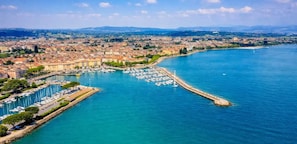 A coastal cityscape with a marina filled with boats, a prominent waterfront promenade, and a backdrop of urban buildings. - la terrazza sui tetti (Desenzano del Garda)