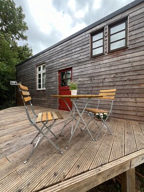 A wooden deck with a table and two chairs, a red door, and a window. - Big Break in the Tiny House on the Farm Near the Baltic Sea (Schashagen)