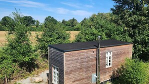 A small wooden cabin with a metal chimney, surrounded by greenery and trees. - Big Break in the Tiny House on the Farm Near the Baltic Sea (Schashagen)