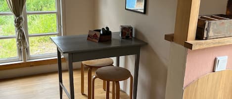 Ein Zimmer mit Holztisch und zwei Hocker, einem fenster mit Vorhängen und einem Spiegel an der Wand.