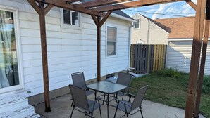 Une terrasse couverte, dotée d’une table et de chaises, jouxtant une maison avec une terrasse en bois et une clôture.