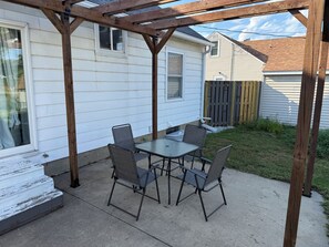 A covered patio with a table and chairs, adjacent to a house with a wooden deck and a fence. - VIP Suite—2BR/1 BA House Near Mayo Clinic Hospital (Rochester)