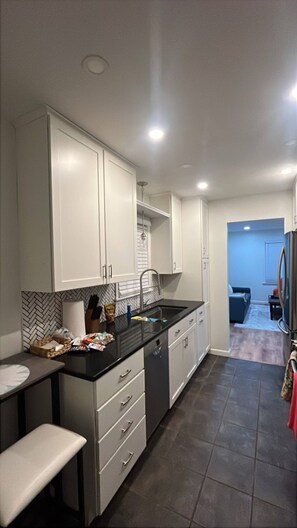 A modern kitchen with white cabinets, a black countertop, and a built-in dishwasher. - VIP Suite—2BR/1 BA House Near Mayo Clinic Hospital (Rochester)