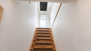 Eine Holztreppe mit schwarzen Teppichläufern, die zu einer Tür oben führt.