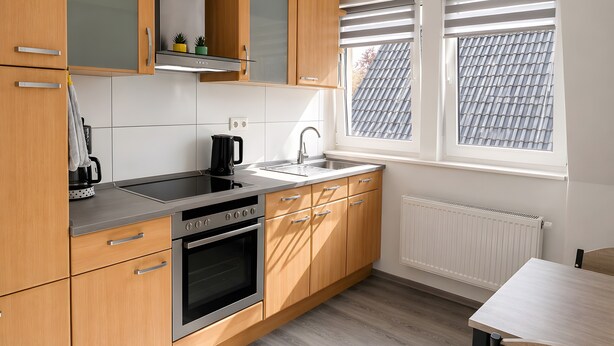 Eine moderne Küche mit Holzschränken, einem Edelstahlherd und einem Fenster mit Jalousien.