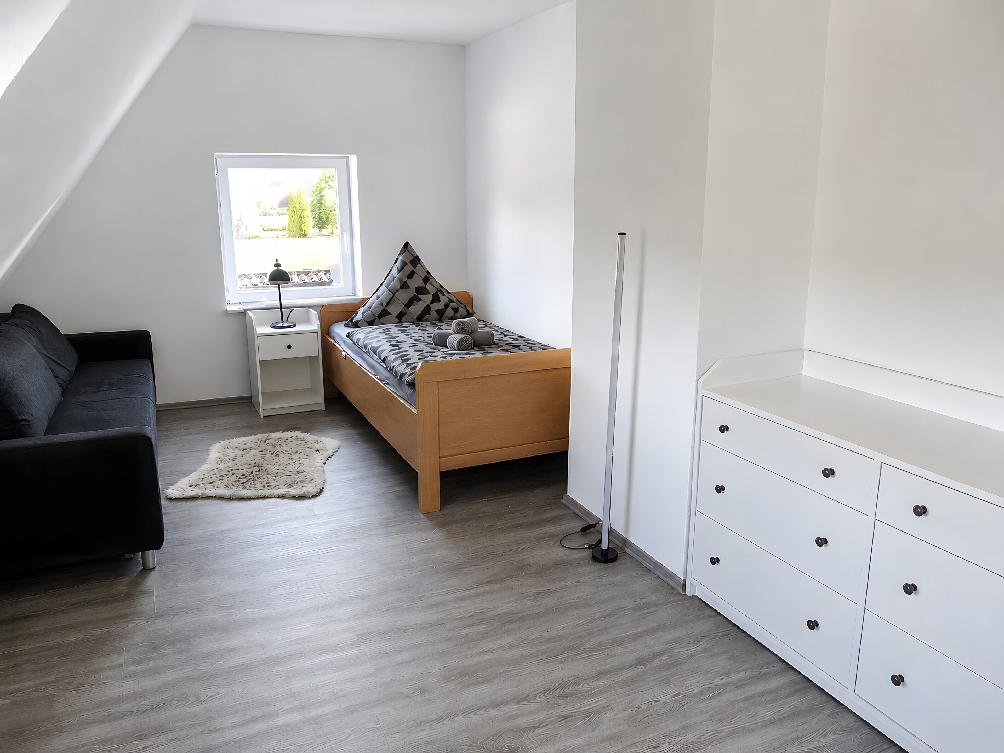 A bedroom with a bed, a desk, a chair, a wardrobe, and a window.