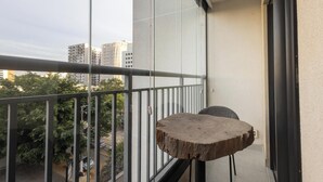 Un balcon avec une table et une chaise en bois, donnant sur un paysage urbain avec des immeubles et des arbres.