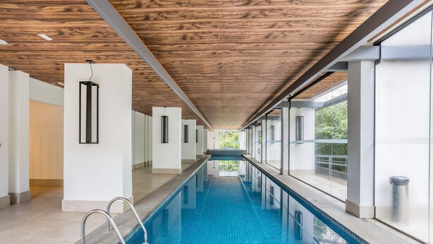 Une piscine intérieure moderne avec un plafond en bois, des murs en verre transparent et un sol carrelé.
