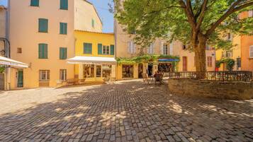 A cobblestone street with buildings, a tree, and outdoor seating.