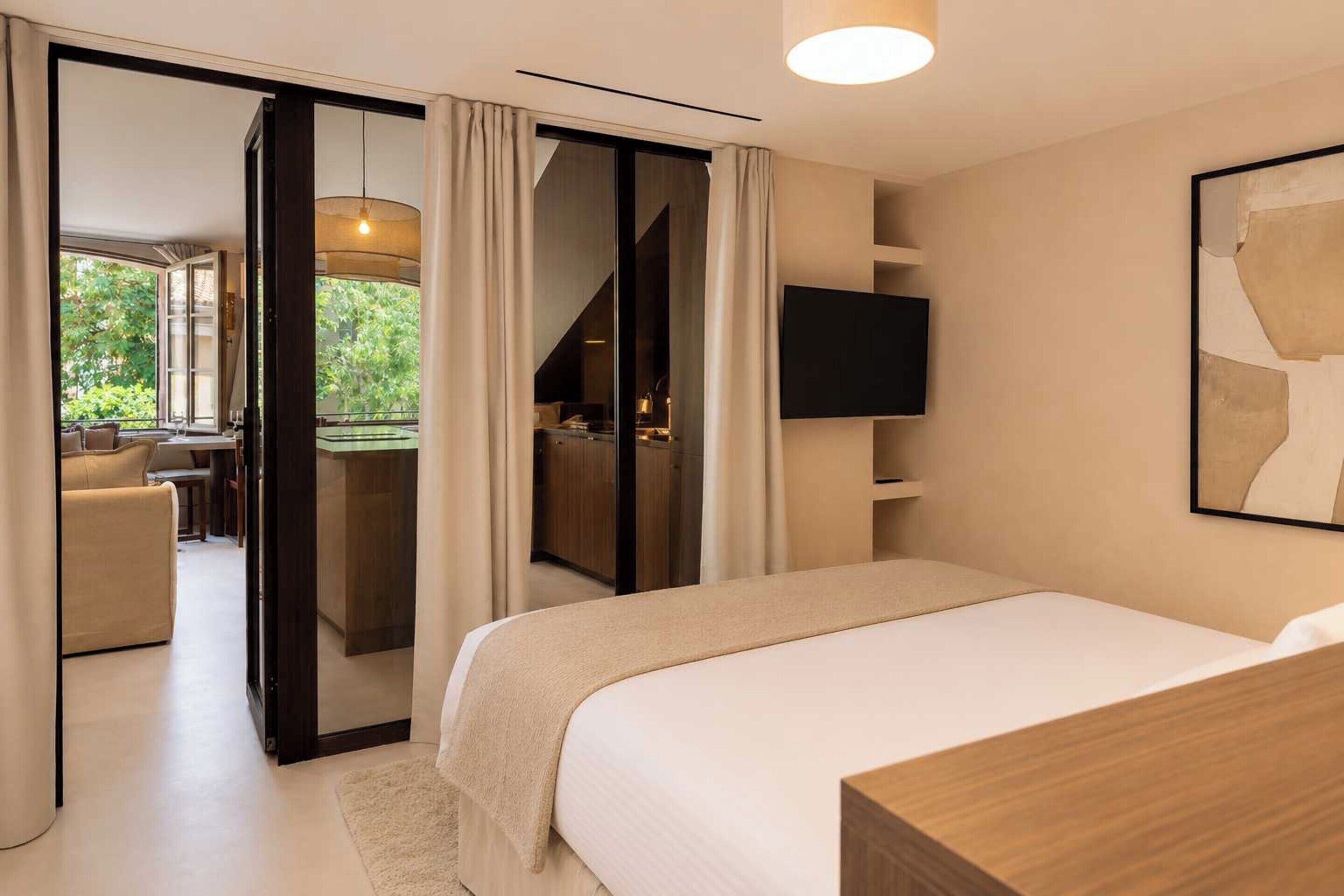 A bedroom with a bed, a TV, and a view of a balcony.