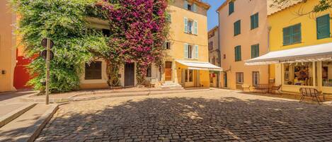 A cobblestone street with buildings, a café with outdoor seating, and a tree with purple flowers.