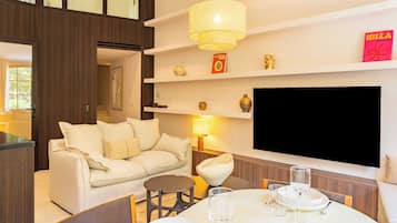 Una sala moderna con un sofá, una mesa de comedor con vasos, un televisor montado en la pared y una estantería con objetos decorativos.