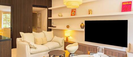 A modern living room with a sofa, a dining table with glasses, a TV mounted on the wall, and a bookshelf with decorative items.