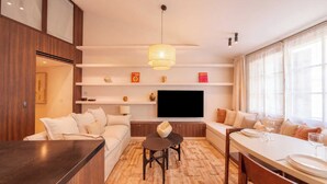 A modern living room with a sofa, a dining table, and a TV mounted on the wall. - Modern 2bdr Flat for 6P - Saint-tropez / Port (Saint-Tropez)