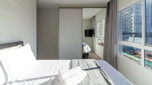 A hotel room with a bed, a television, and a view of a cityscape through large windows. - Apartment in Condominium Near the Beach Pmr0501 (Porto Belo)
