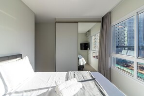 Ein Hotelzimmer mit Bett, Fernseher und Blick auf eine Stadtlandschaft durch große Fenster.