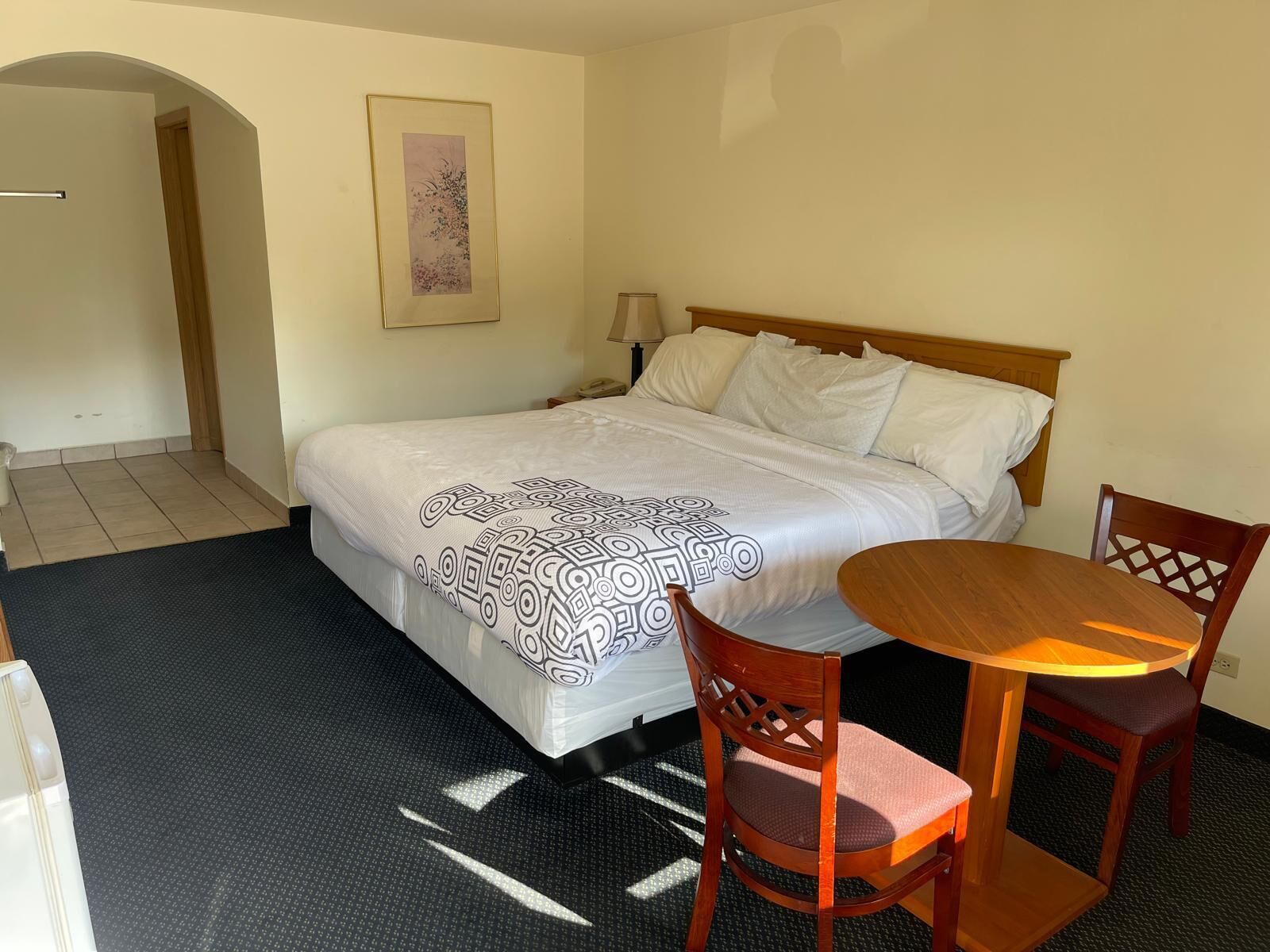 Hotellihuone, jossa on sänky, yöpöytä, lamppu, tuoli ja pieni pöytä.