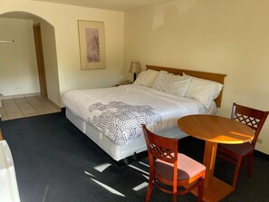A hotel room with a bed, a bedside table, a lamp, a chair, and a small table. - D-Lux budget Inn (Lemont)