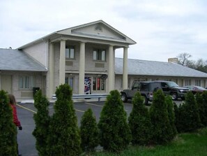 A building with a classical architectural style, featuring a central entrance with columns, a parking lot, and a few vehicles. - D-Lux budget Inn (Lemont)