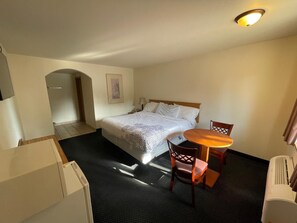 Habitación de hotel con una cama, una pequeña mesa con sillas, un escritorio, una silla y un televisor montado en la pared.