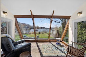 Ein Zimmer mit einem großen Fenster, einem schwarzen Ledersessel, einem gemusterten Teppich und einem kleinen Zierhocker.