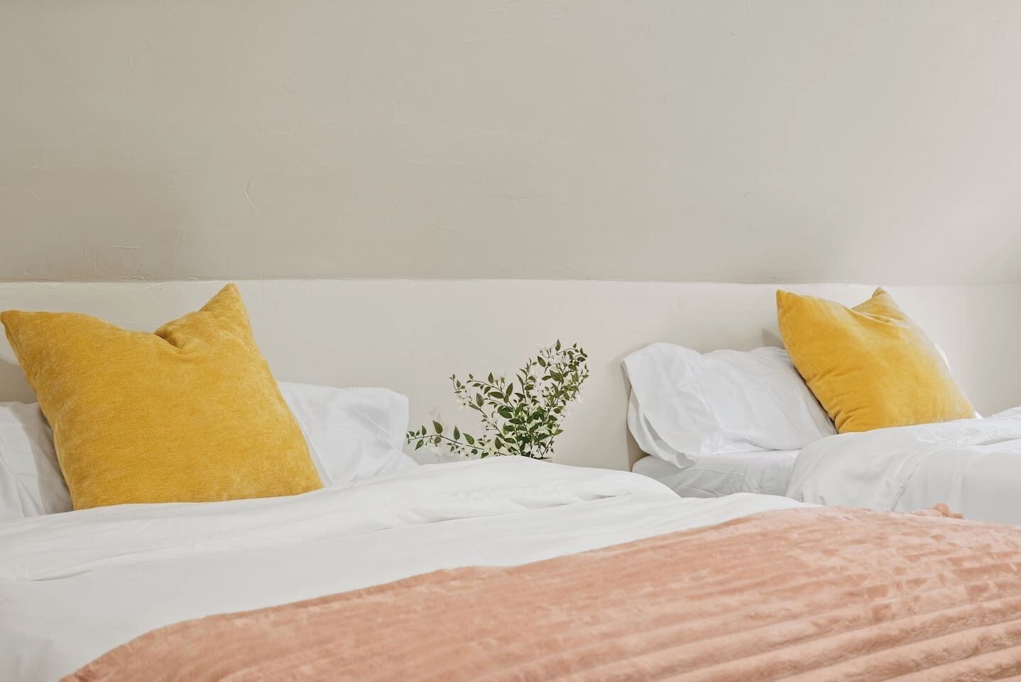 A hotel room with two beds, each with white bedding and a single yellow pillow.