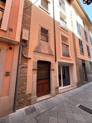 Un edificio con fachada de piedra, puerta de madera y balcón de metal.