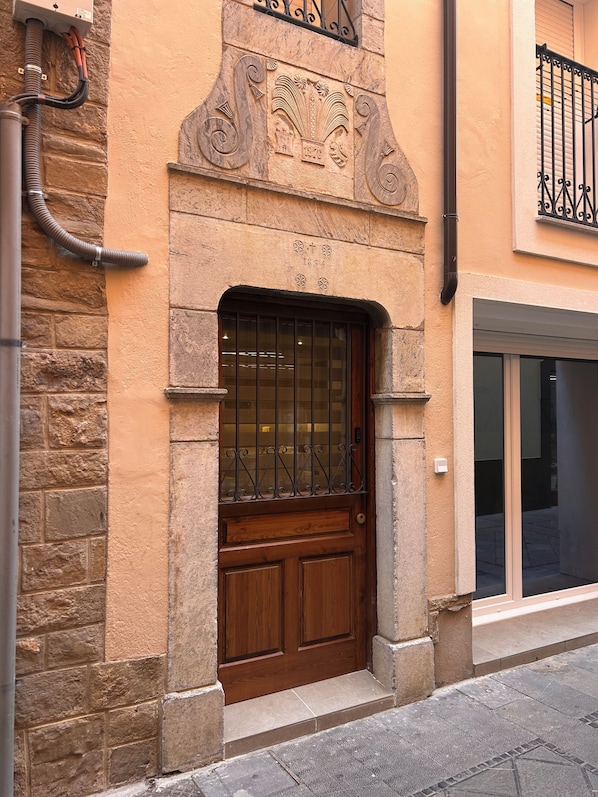 A building facade with a wooden door, a window with metal bars, and a stone wall.