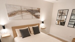 Un dormitorio con una cama grande, dos mesitas de noche, una mesilla auxiliar, una lámpara de pared y una lámpara de pie.