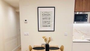 Un comedor con una mesa de madera, individuales negros y sillas. Hay una obra enmarcada en la pared sobre la mesa.