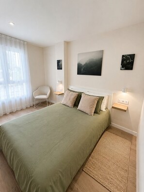 A bedroom with a large bed, a chair, a bedside table, and a wall-mounted shelf.