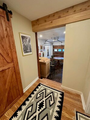 Un pasillo con piso de madera, un tapete estampado y una puerta que da a un comedor con una mesa redonda y sillas.