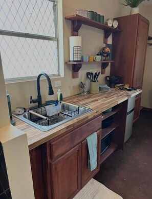 Una cocina con armarios de madera, un lavamanos doble y una ventana con mosquitero.