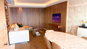 Una sala moderna con un sofá blanco, una mesa de comedor con sillas, una mesa de centro y un televisor instalado en la pared.