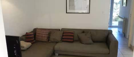 A living room with a sectional sofa, a framed picture on the wall, and a tiled floor.