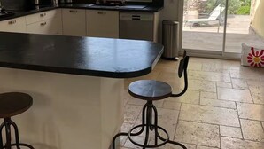 A modern kitchen with a central island, bar stools, and a view of a garden through a sliding glass door. - Family Home - Peaceful, with a Pool and Surrounded by Nature, 4 km from the Sea (Fréjus)