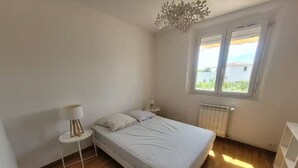 A bedroom with a bed, a bedside table, a lamp, a radiator, and a window with a view. - Family Home - Peaceful, with a Pool and Surrounded by Nature, 4 km from the Sea (Fréjus)