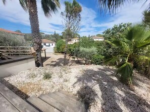 Eine Terrassenfläche mit Holzboden, Kiesgrund und verschiedenen Pflanzen, darunter Palmen.
