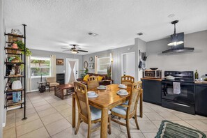 A modern kitchen with a dining area, featuring a wooden table, chairs, and a built-in oven. - The Landing Pad | Pet Friendly Yard (Tampa)