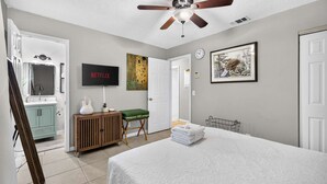 A bedroom with a bed, a ceiling fan, a television, a painting, and a door. - The Landing Pad | Pet Friendly Yard (Tampa)