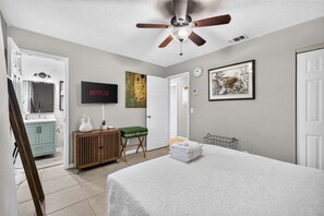 A bedroom with a bed, a ceiling fan, a television, a painting, and a door. - The Landing Pad | Pet Friendly Yard (Tampa)