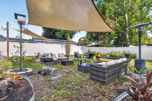 An outdoor patio area with wicker furniture, a barbecue grill, and a table with chairs. - The Landing Pad | Pet Friendly Yard (Tampa)