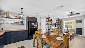 A modern kitchen with a dining area, featuring a black refrigerator, wooden cabinets, and a dining table with chairs. - The Landing Pad | Pet Friendly Yard (Tampa)