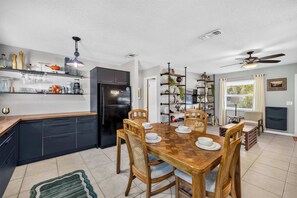A modern kitchen with a dining area, featuring a black refrigerator, wooden cabinets, and a dining table with chairs. - The Landing Pad | Pet Friendly Yard (Tampa)